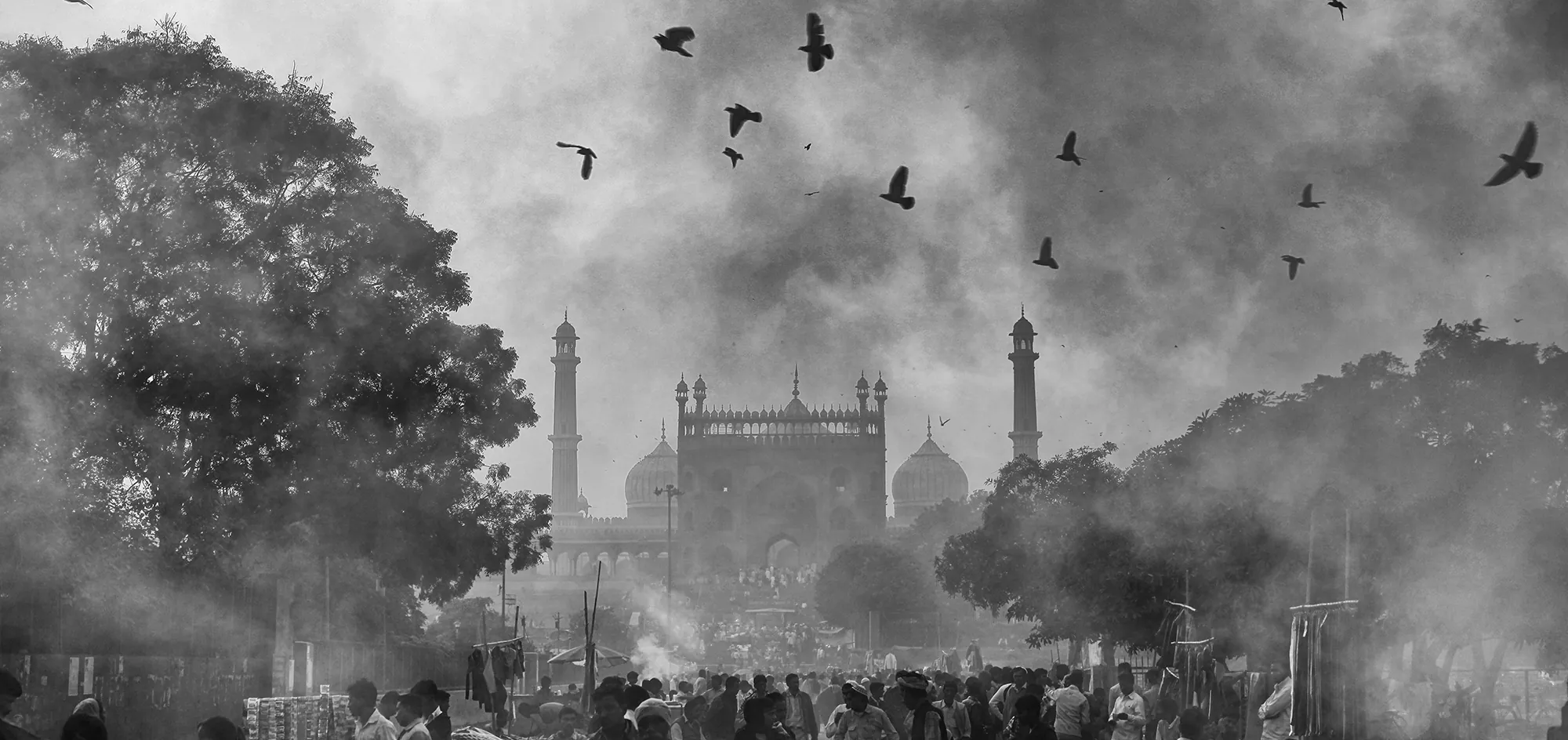 Jama Masjid silhouetted in morning haze, birds circling above its domes and minarets.