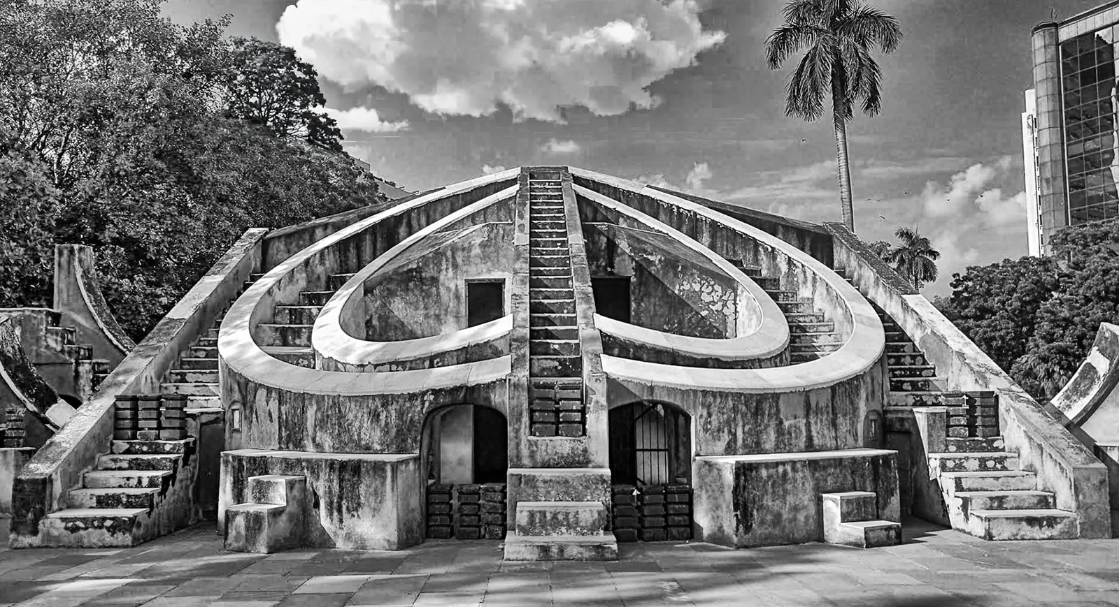 The giant curved masonry instrument at Jantar Mantar, twin staircases climbing its walls under a dramatic sky.