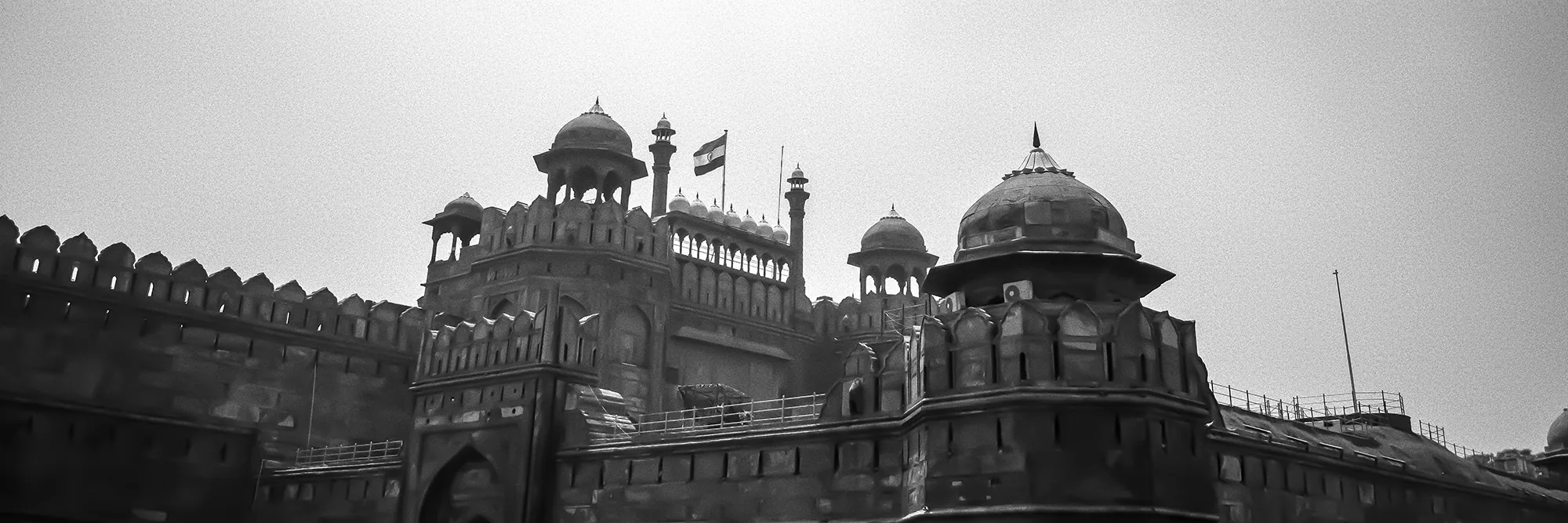 The sandstone ramparts and domed gatehouse of the Red Fort, the Indian flag flying above the Lahore Gate.
