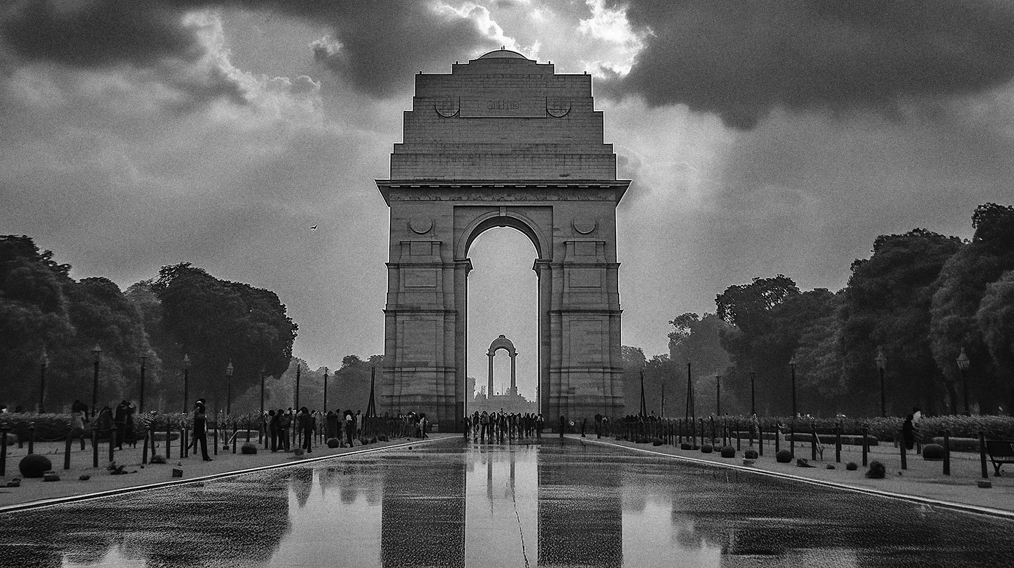 India Gate under a brooding monsoon sky, its arch reflected in the rain-slicked boulevard.